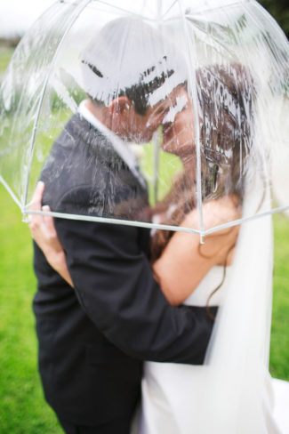 newlyweds kiss under clear umbrella