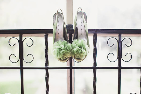 Green wedding shoes with giant green pompoms, hanging from iron railing