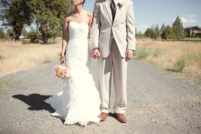 bride and groom stand in gravel road holding hands
