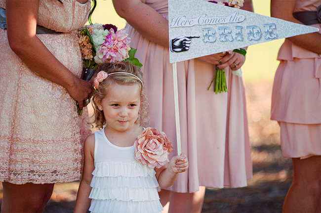 flower girl holding pennant that says "here comes the bride"