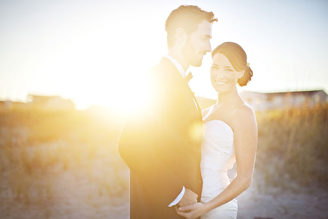 newlyweds on beach with sun setting behind them