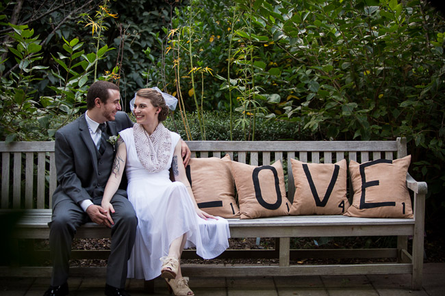 bride and groom sit on bench at Klein-Pringle White Garden with pillows that spell LOVE