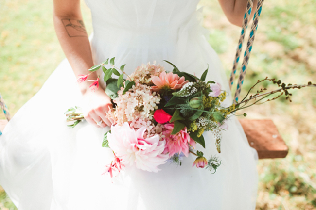 close up photo of bride sitting on wooden swing holding colorful bridal bouquet