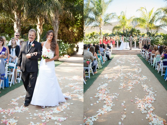 Bride walking down aisle with father outside with scattered flower petal