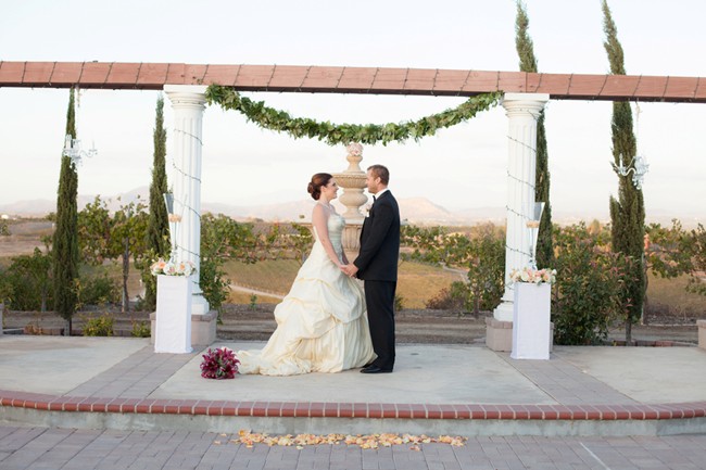 bride and groom standing at altar at Mount Palomar Winery with peach rose petals and fountain