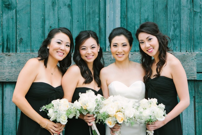 Bride standing with bridesmaids wearing black strapless dresses standing in front of turquoise wall 