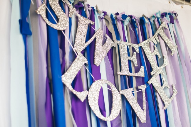 Silver sparkle sign spelling out "sweet love" with purple, blue and mauve crepe paper hanging for background