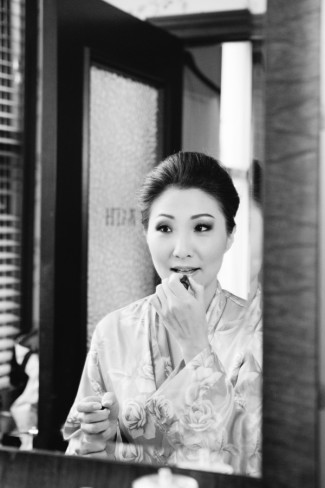 Black and white photo Korean bride putting lipstick on in the mirror wearing silk robe 