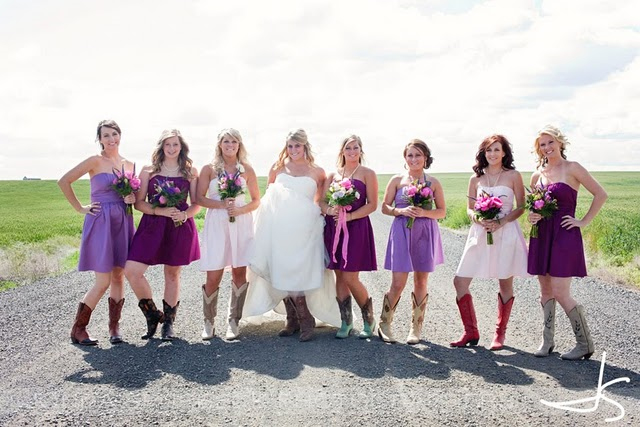 Bride standing on a country road with bridesmaids who are wearing purple mismatched dresses and all wearing cowboy boots 