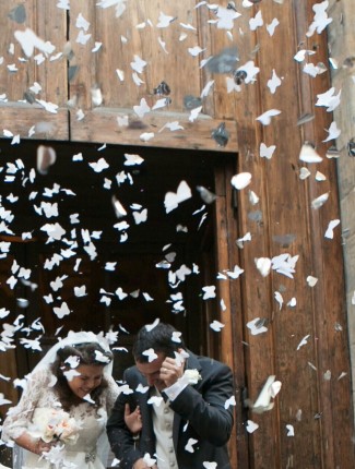 Bride and groom covering as paper confetti fall from the sky