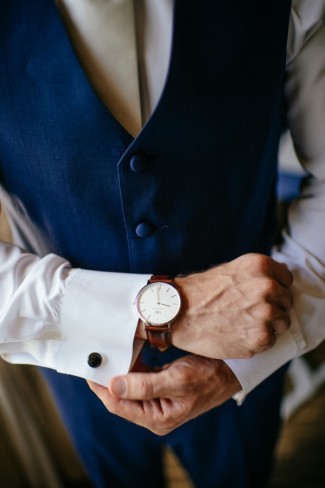Groom wearing blue vest cuff links and a brown watch