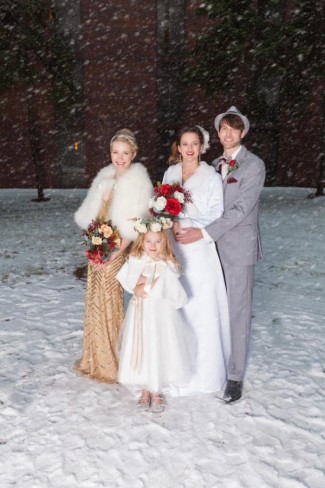 Bride and groom standing outside with maid of honor and flower girl with snow falling down