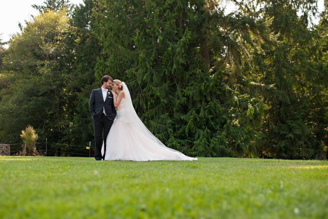 Bride wearing a David Tutera gown posing with groom in lawn. 