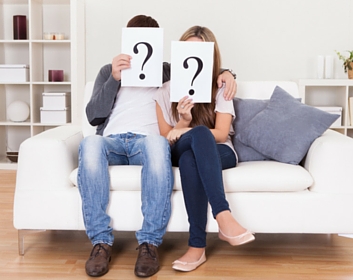 couple on couch holding question marks in front face