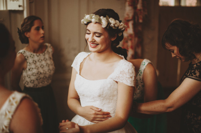 Bride smiling holding her stomach with her eyes closed wearing a flower crown made by whichgoose