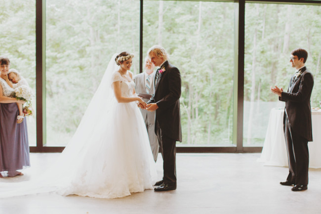 bride and groom holding hands during wedding ceremony in front of a big window