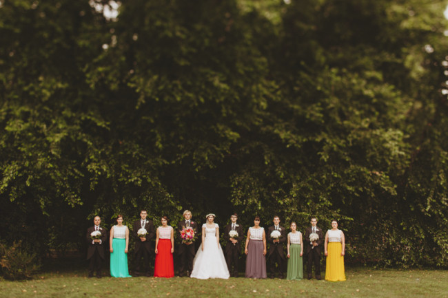 Bridal party standing in a line with bridesmaids wearing mismatched bright skirts and groomsmen in formal morning coats