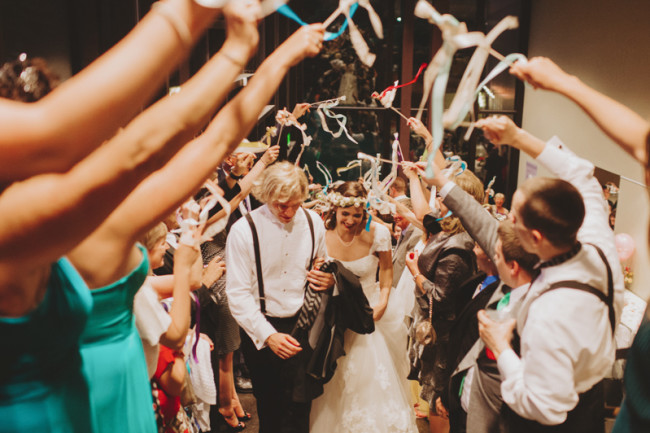Bride and groom walking between guests who are throwing bright ribbons at them