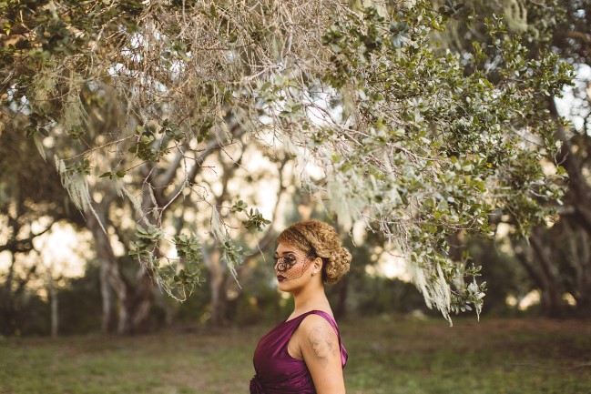 model in purple dress and black birdcage veil outdoors under tree branch