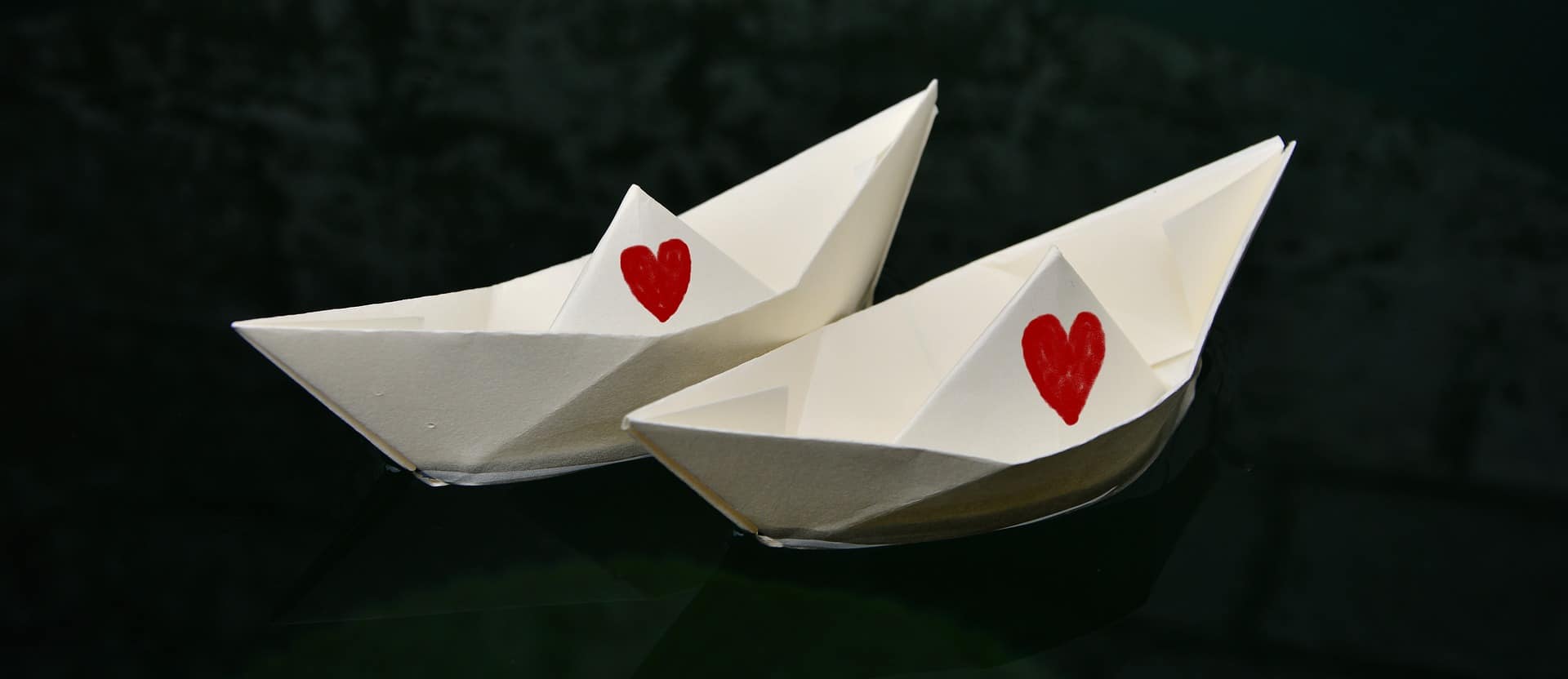 2 paper boats in the water with red hearts