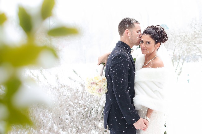 groom with bride in white shawl as snow falls