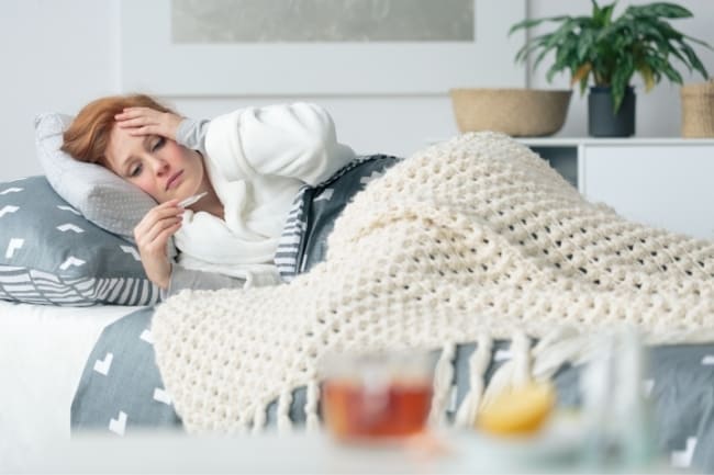 woman sick in bed taking temperature
