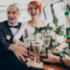 stylish happy bride and groom toasting with glasses of champagne and having fun with bridesmaids and groomsmen inside of retro car. emotional moment, space for text. wedding party