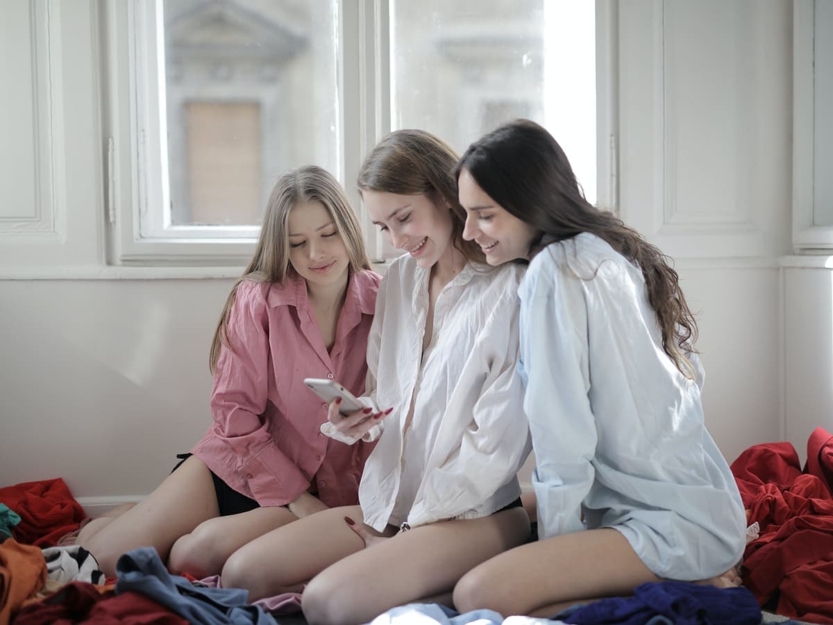 Group of young women browsing smartphone together in messy room