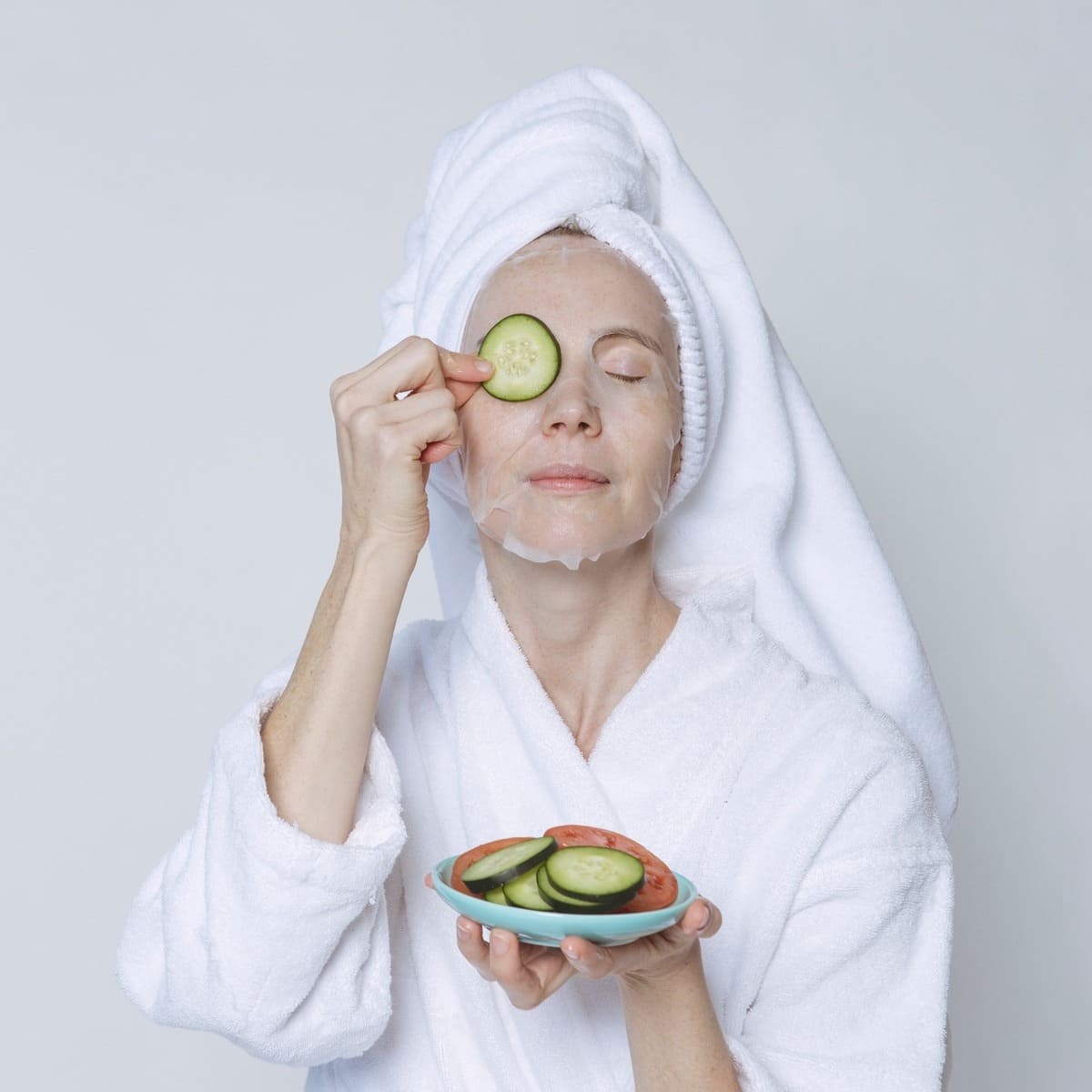 Woman in sheet mask covering eyes with cucumber slices
